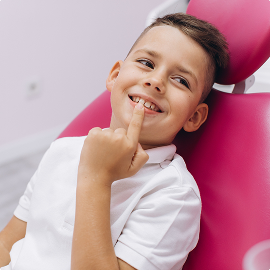 Young boy in the dental chair pointing to his teeth