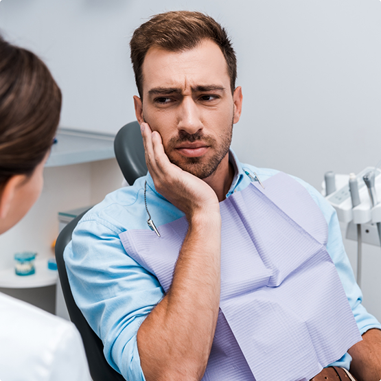 Man holding the side of his face in pain while talking to his orthodontist