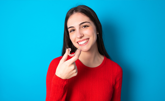 Smiling young woman in a red blouse holding Invisalign