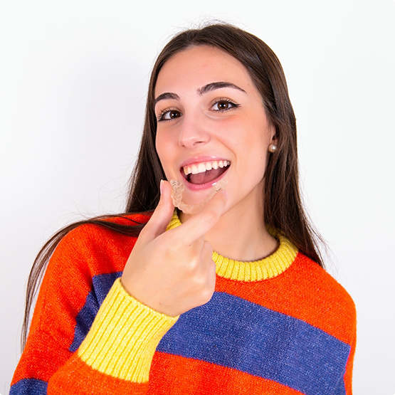 Teenage girl holding an Invisalign clear aligner near her smile