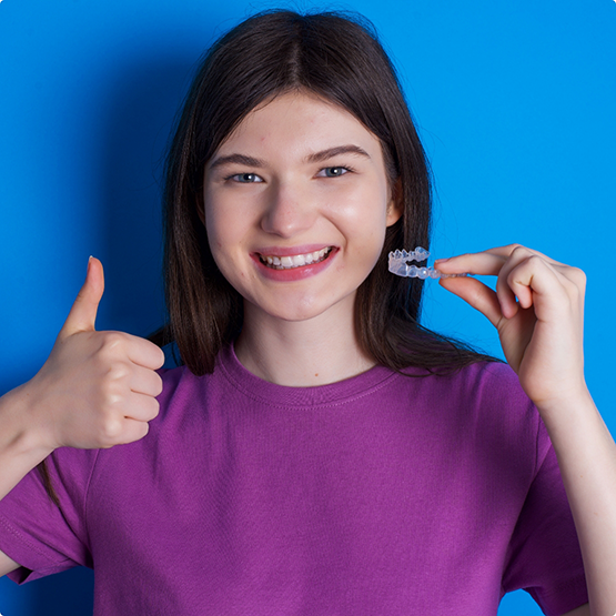 Young woman holding an aligner and giving a thumbs up