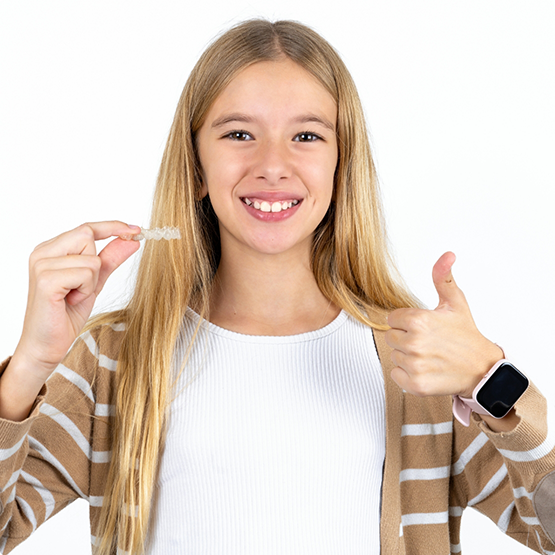 Blonde teenage girl smiling and giving a thumbs up while holding Invisalign