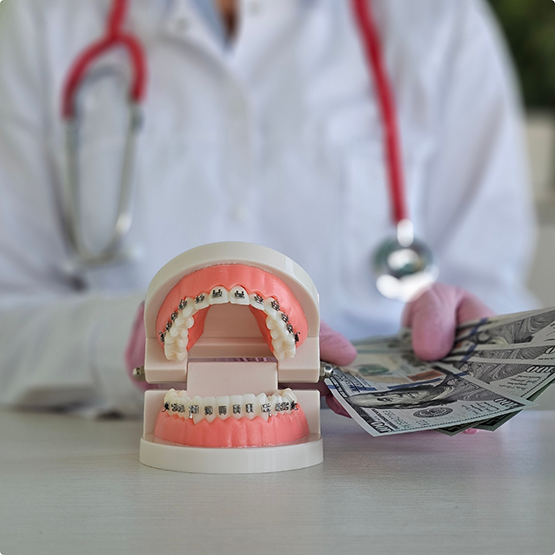 Orthodontist holding several dollar bills at a desk next to a model of the teeth