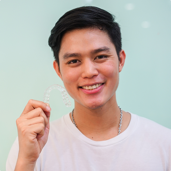 Smiling young man holding an Invisalign tray