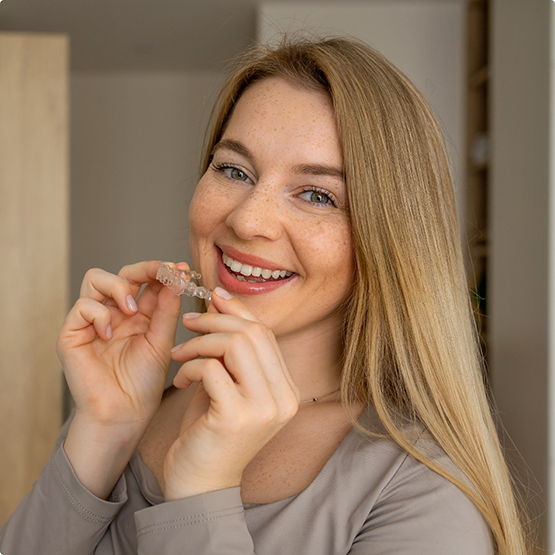 Blonde woman holding Invisalign close to her smile