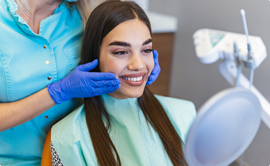 Young woman in the treatment chair looking at her smile in a mirror