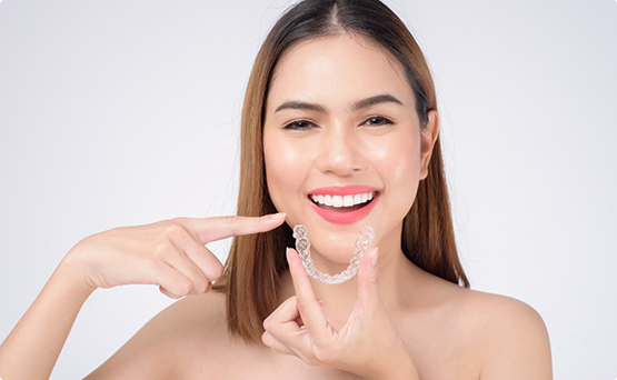 Woman holding Invisalign with one hand and pointing to her smile with the other