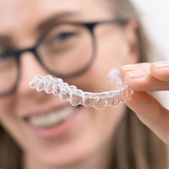Smiling woman with glasses holding an Invisalign aligner